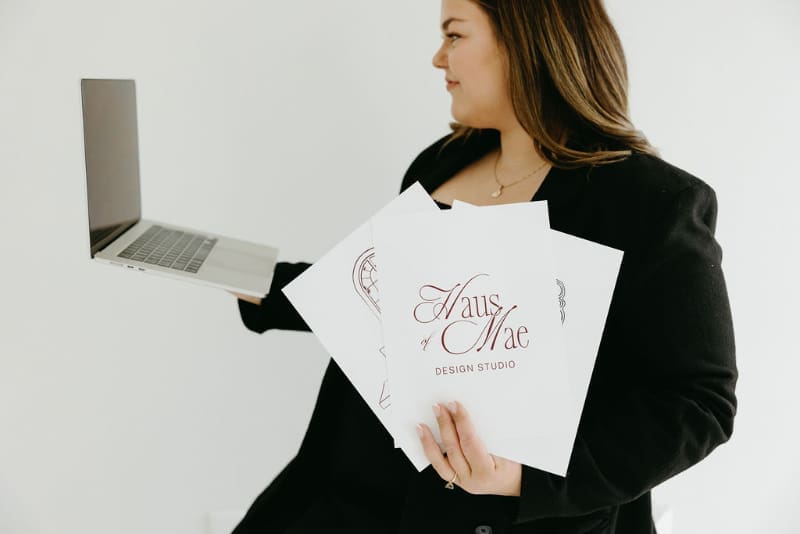 Creative business owner holding laptop and branding sheets, Showit vs Squarespace website design decision visual