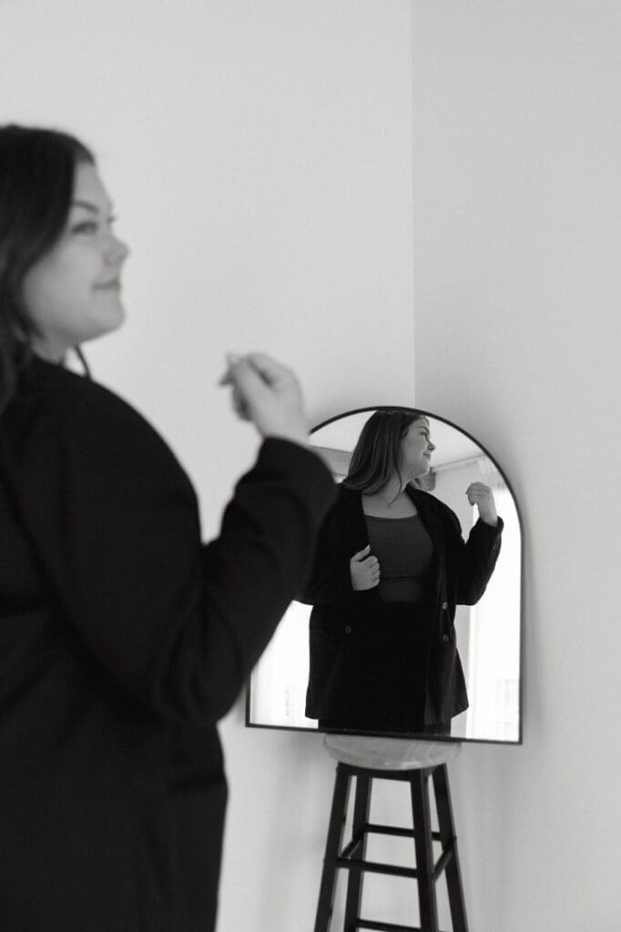 Business owner adjusting blazer in mirror while planning intentional website updates for her brand.